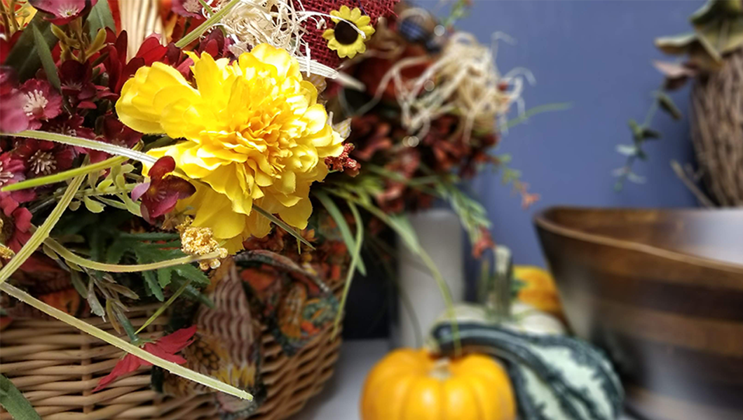 Fall foliage in a basket in the foreground, focused on a bright yellow calendula flower with a Wavy Rim Bowl in Walnut finish from Lipper International in the background