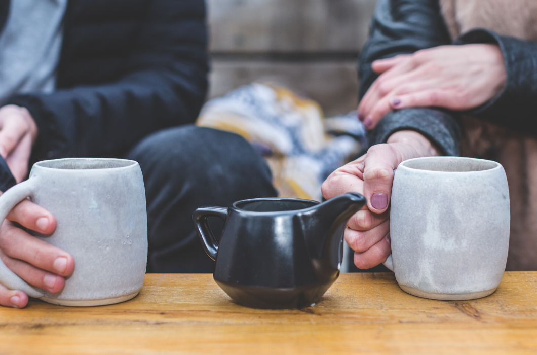 Photograph: A Close up of two teacups on a table being held by a man and a woman sitting on a couch talking