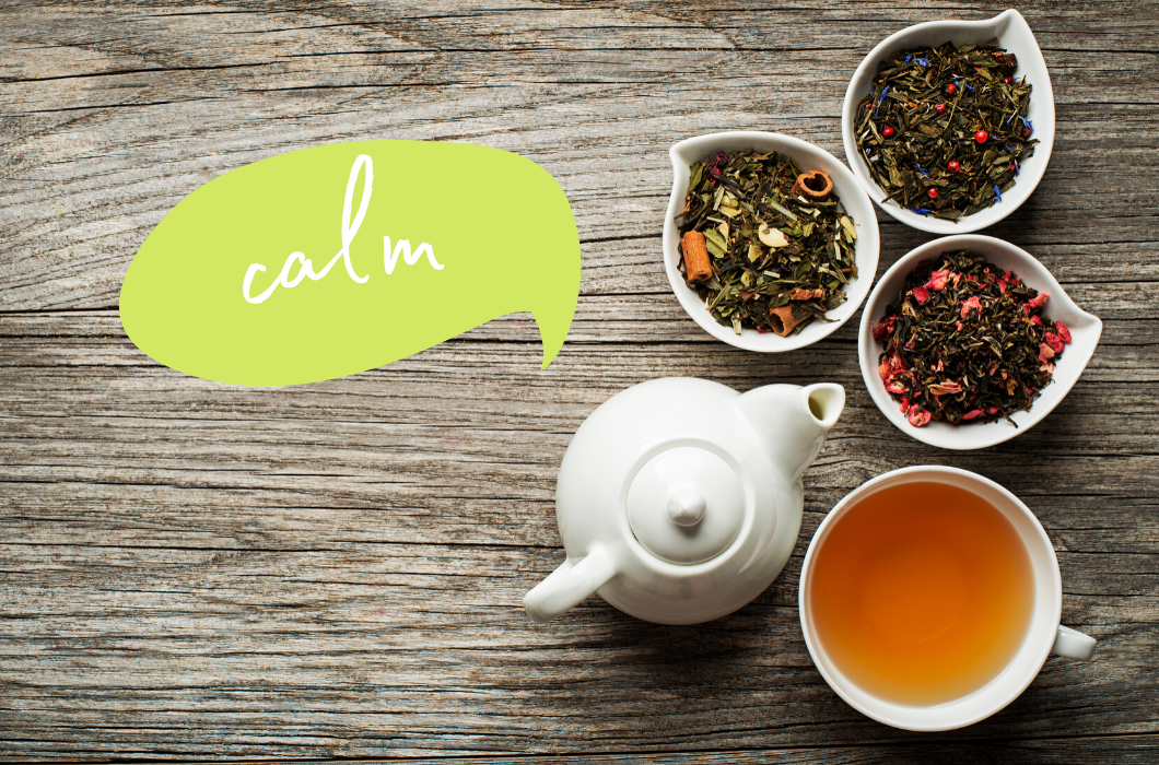 Photograph: An overhead shot of a small white tea pot and two small white dishes of loose leaf tea on a weathered gray wood background. There is a green speech bubble coming out of the teapot with the word 