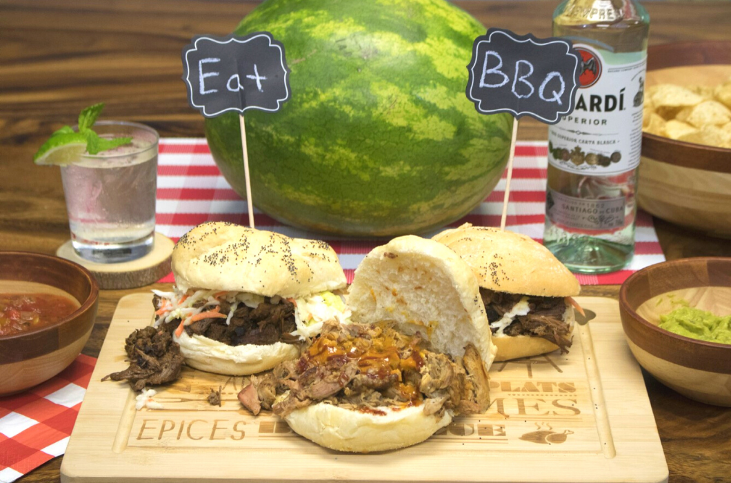 Photograph of Lipper International Item 8955, a BBQ themed cutting board, with pulled pork sliders on it, a watermelon, and two small table signs that read 