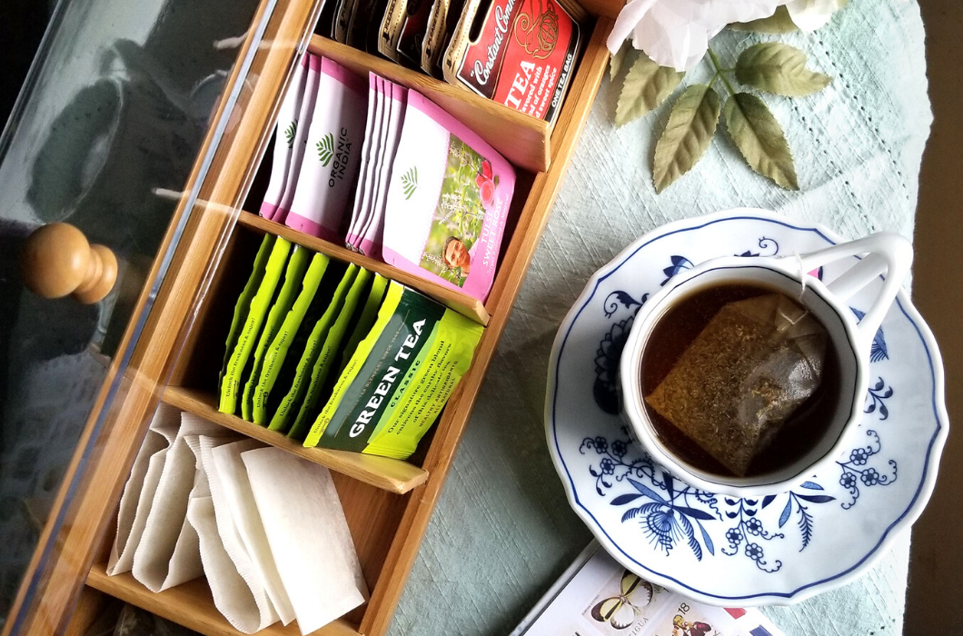 Lipper International Item 8187 clear acrylic tea box with tea bags and a cup of tea on a table from above