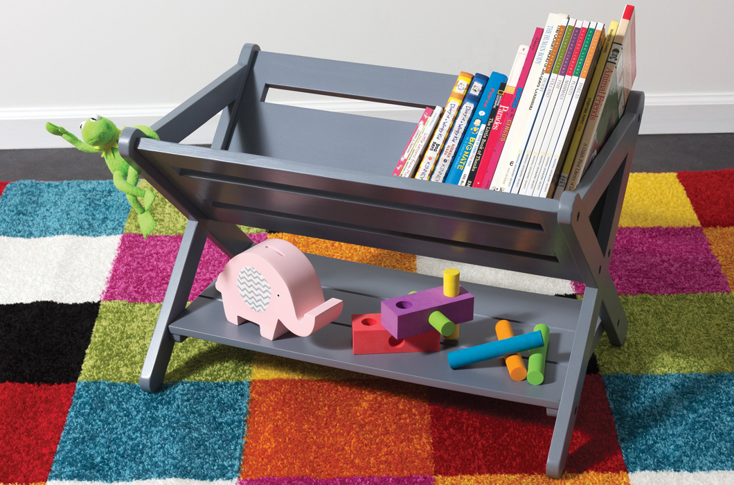 Lipper International Item 522, The Kids Book Caddy, in Gray, on top of a colorful checkered rug and with fun kids books and toys in it. 