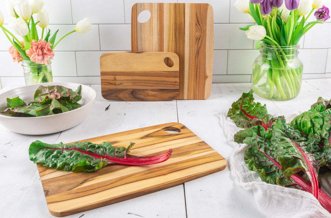 Lipper International Item 7239, Set of 3 Edge Grain Teak Cutting Boards in a brightly lit kitchen with salad ingredients and a vase of flowers